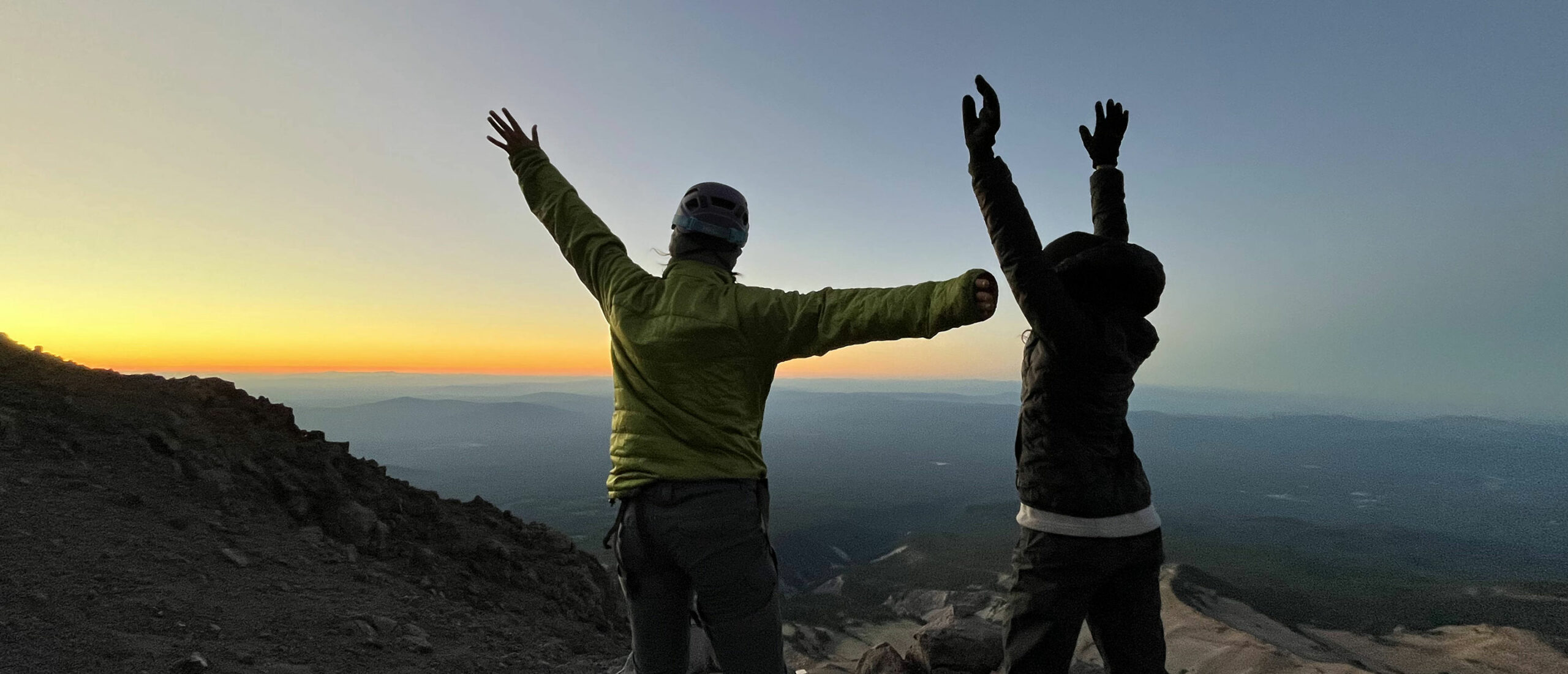 teenagers standing on top of the mountain mount shasta with arms raised at sunrise