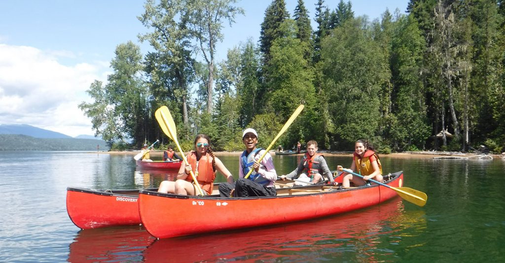 teenagers holding paddles in red canoes on lake