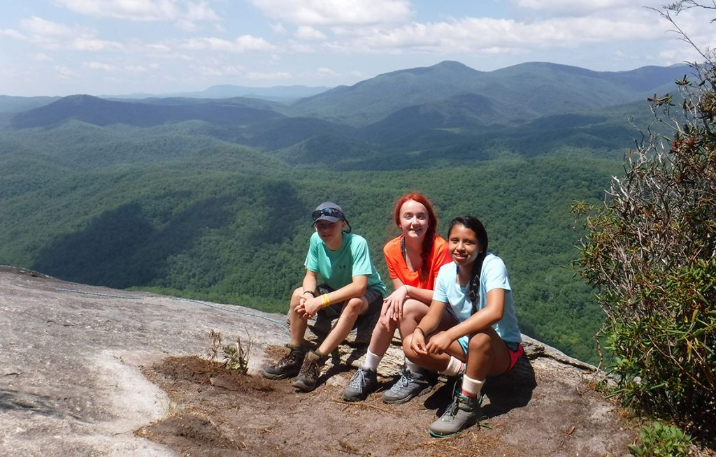 teenagers sitting on rock face in mountains with view