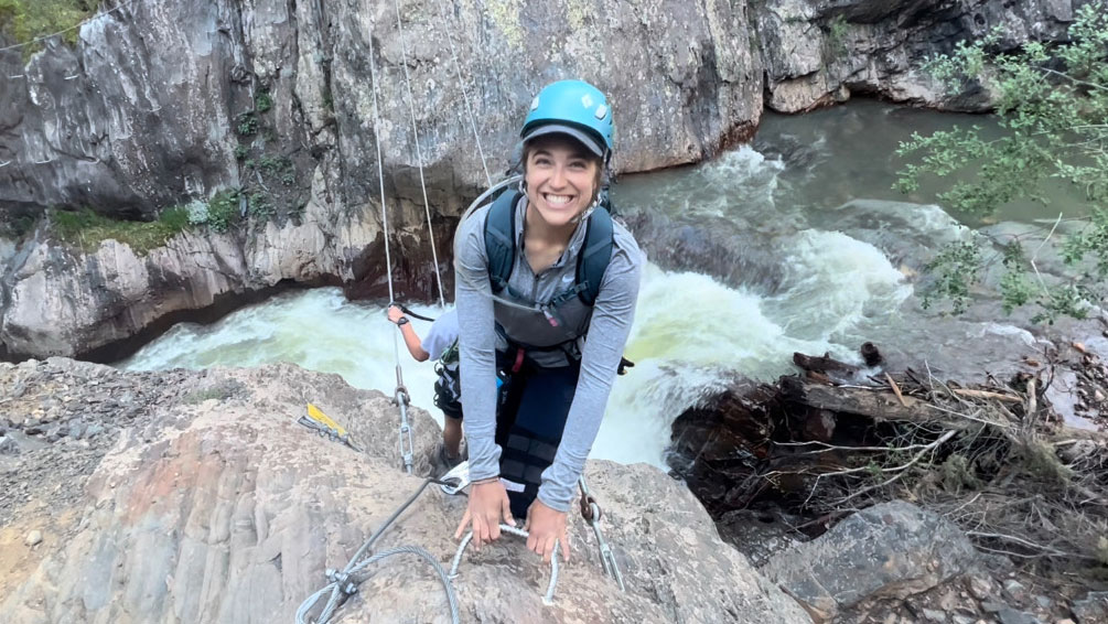 woman rock climbing above a river wearing a helmet