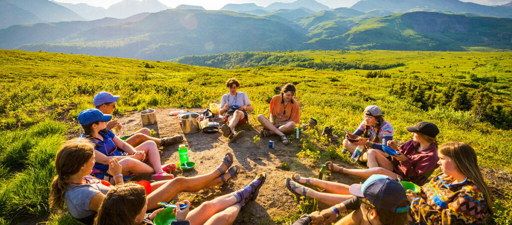 Hikers sitting around in a circle with mountains in the background.
